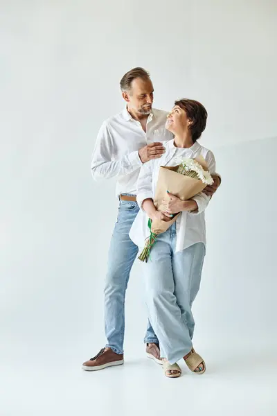 Vollständige Aufnahme eines Paares mittleren Alters mit Blumen auf grauem Hintergrund, die sich gegenseitig anschauen — Stockfoto