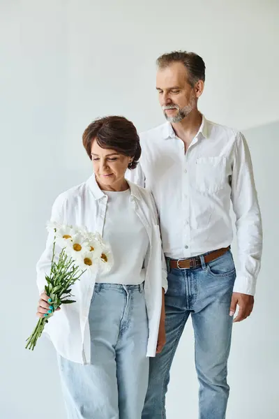 Portrait of happy mature couple standing together with flowers on grey background, present — Stock Photo