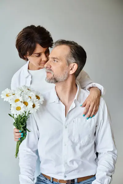 Attraktive Frau hält Blumen in der Hand und umarmt reifen Mann in weißem Hemd auf grauem Hintergrund — Stockfoto