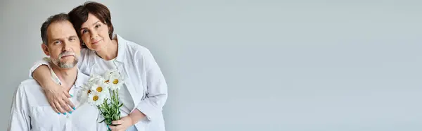 Porträt eines Paares mittleren Alters mit Blumen auf grauem Hintergrund, Frau stützt sich auf Mann, Banner — Stockfoto