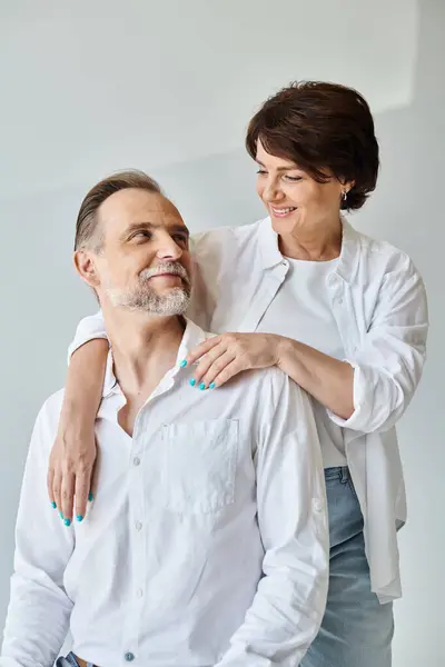 Attraente donna di mezza età che abbraccia l'uomo maturo in camicia bianca con amore su sfondo grigio — Foto stock