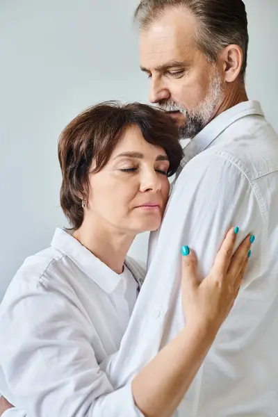 Seitenansicht Porträt eines Paares mittleren Alters, das sich vor grauem Hintergrund mit geschlossenen Augen umarmt — Stockfoto