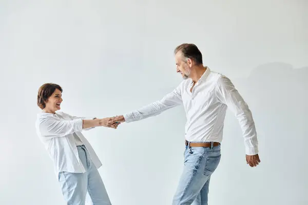 Side view portrait of middle aged couple in love dancing cheerfully on grey backdrop — Stock Photo