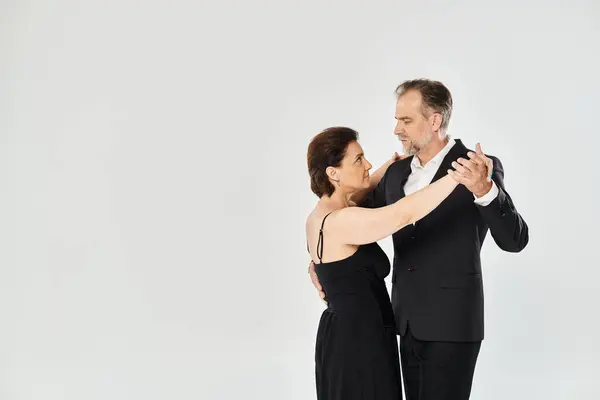 Uma mulher de vestido preto e homem de terno escuro abraçando em fundo cinza, em pose de tango — Fotografia de Stock