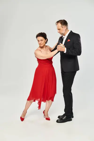 Image pleine longueur de couple attrayant mature en robe rouge et costume dansant sur fond gris — Photo de stock