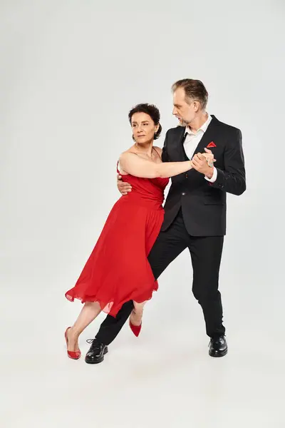 Danse de salon couple d'âge moyen en robe rouge et costume danse tango isolé sur fond gris — Photo de stock