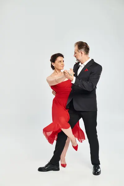 Danse de salon couple d'âge moyen en robe rouge et costume danse tango isolé sur fond gris — Photo de stock