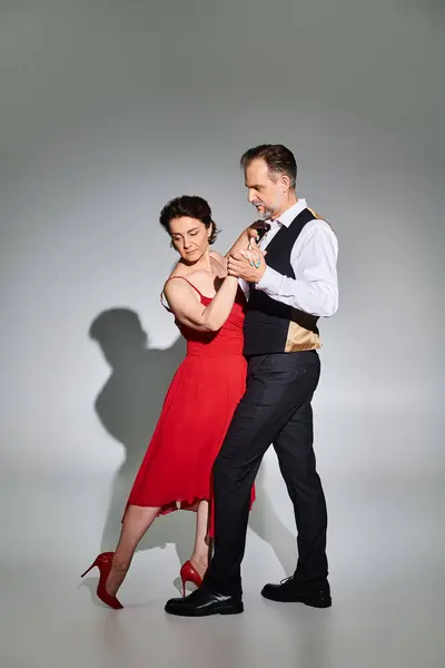 Danse de salon couple d'âge moyen en robe rouge et costume danse tango isolé sur fond gris — Photo de stock