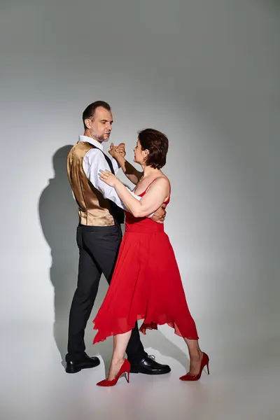 Danse de salon couple d'âge moyen en robe rouge et costume danse tango isolé sur fond gris — Photo de stock