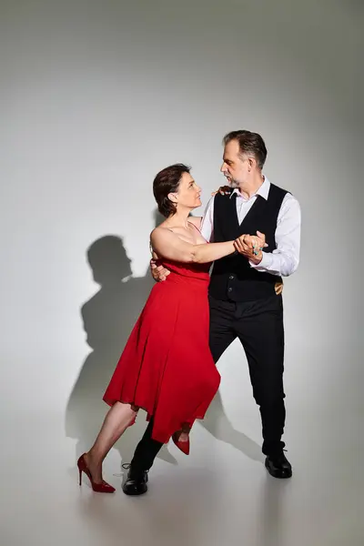 Danseurs couple souriants attrayants d'âge moyen en robe rouge et costume performant sur fond gris — Photo de stock