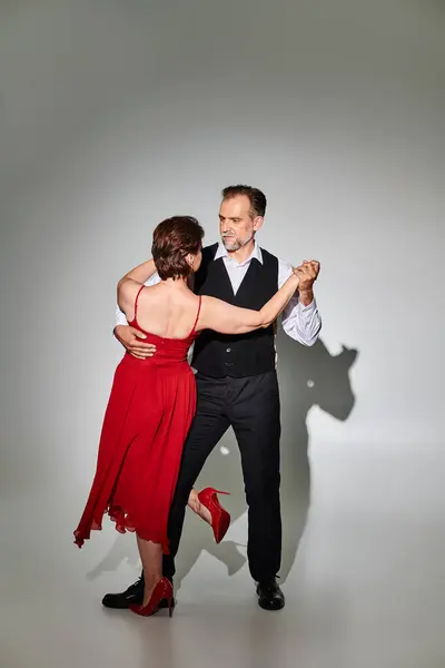 Imagen de pareja de bailarines de tango maduros en traje y vestido rojo actuando sobre fondo gris - foto de stock