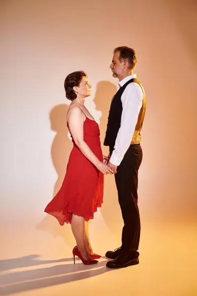 Mediana edad atractiva pareja sonriente bailarinas en vestido rojo y traje con luz amarilla sobre gris - foto de stock