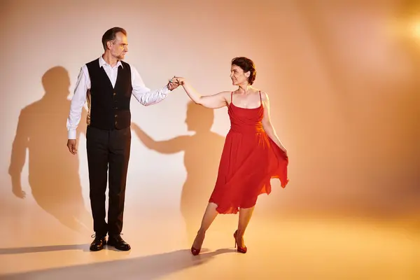 Бальний танець середнього віку пара в червоній сукні і костюм танцює танго з жовтим світлом на сірому — стокове фото