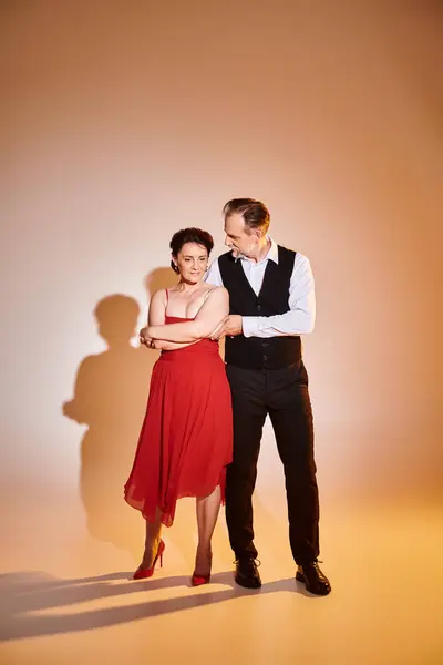 Danseurs couple souriants attrayants d'âge moyen en robe rouge et costume avec lumière jaune sur gris — Photo de stock