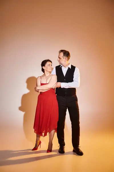 Retrato de pareja atractiva de mediana edad en vestido rojo y traje de pie sobre fondo gris - foto de stock