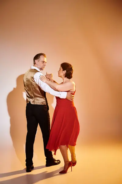 Danse de salon couple d'âge moyen en robe rouge et costume danse tango avec lumière jaune sur gris — Photo de stock