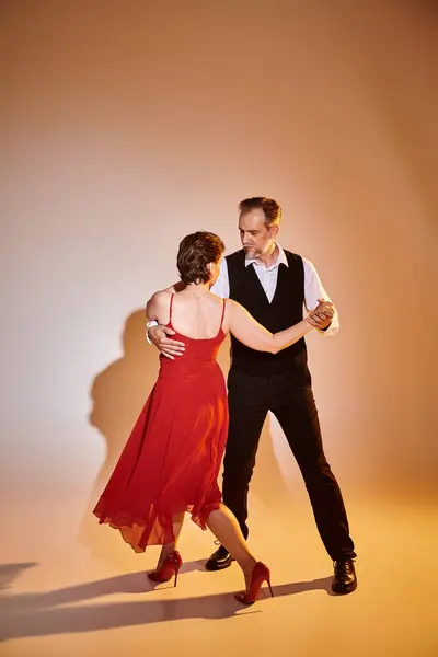 Imagen completa de pareja atractiva madura en vestido rojo y traje bailando sobre fondo gris - foto de stock