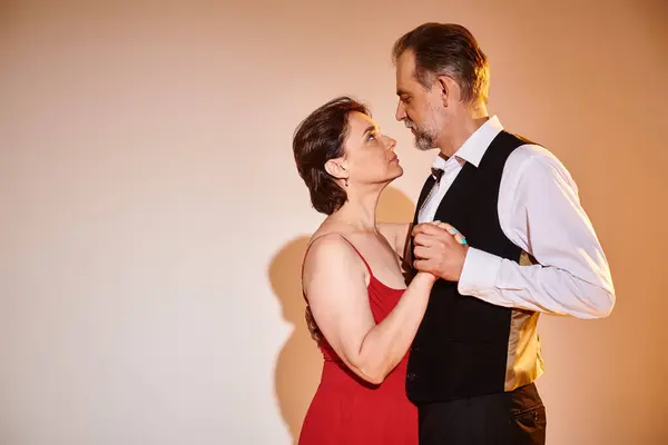 Vista lateral de pareja madura de baile de salón en vestido rojo y traje bailando tango sobre fondo gris - foto de stock