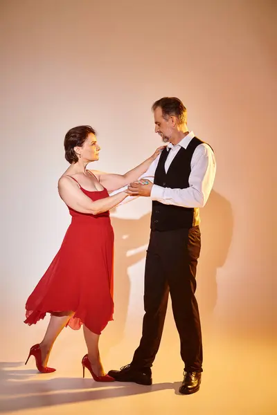 Imagem de comprimento total de casal atraente maduro em vestido vermelho e terno dançando no fundo cinza — Fotografia de Stock