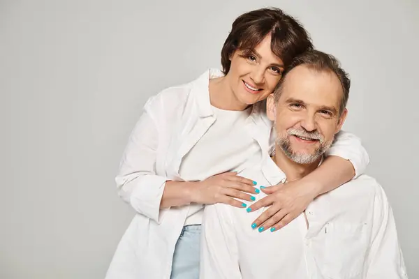 Porträt eines Paares mittleren Alters, das sich umarmt und in die Kamera blickt, lächelnd auf grauem Hintergrund — Stockfoto