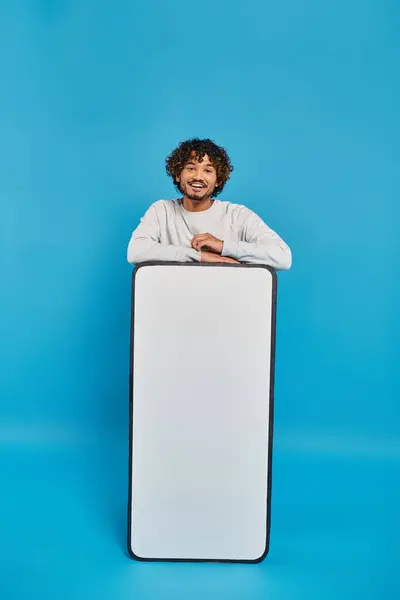 Un homme se tient caché derrière un gros objet blanc dans un décor studio sur fond bleu. — Photo de stock