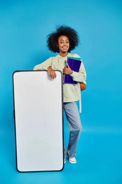 Una mujer sosteniendo un libro y de pie junto a una maqueta de teléfonos inteligentes, listo para embarcarse en una aventura. - foto de stock