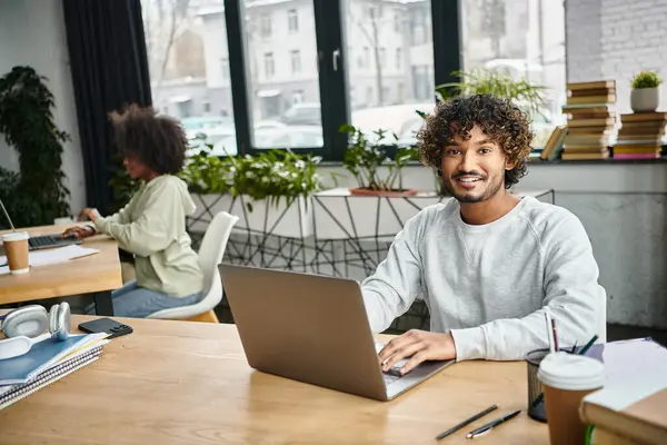 A man of diverse background sits at a table, intensely focused on his laptop in a modern coworking space. — Stock Photo