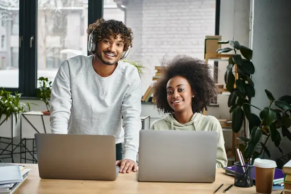 A man and a woman of different ethnic backgrounds sit in a modern coworking space, each focused on their laptops. — Stock Photo