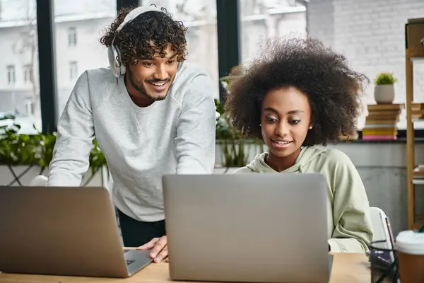 A man and a woman of diverse backgrounds focus intently on a laptop screen in a modern coworking space. — Stock Photo