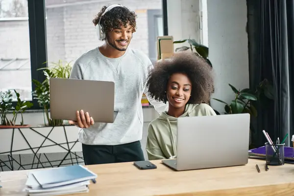 A multicultural man and woman focused on laptops, collaborating in a modern office coworking space. — Stock Photo