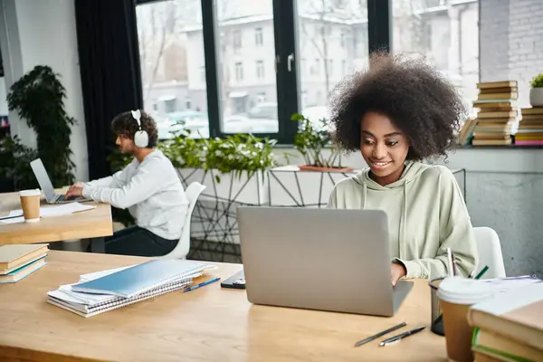 Una donna di diversa provenienza focalizzata sul suo computer portatile in un moderno spazio di coworking tra gli altri studenti multiculturali. — Foto stock
