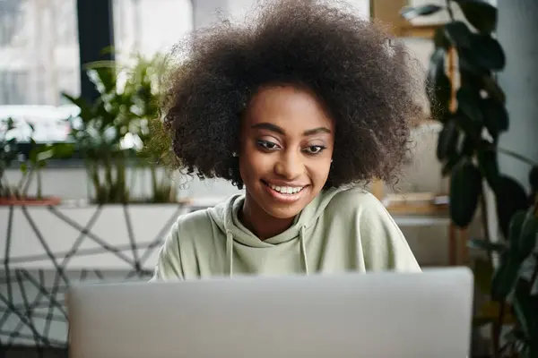 Una donna nera assorbita nel lavoro, seduta di fronte a un computer portatile in un moderno spazio di coworking. — Foto stock