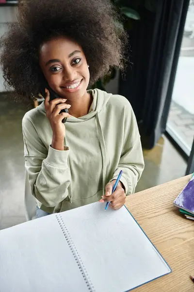 Uma mulher negra envolvida em um telefonema enquanto sentada em uma mesa dentro de casa. — Fotografia de Stock