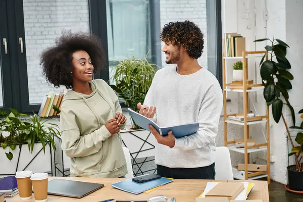 A man and woman stand in a modern office, working together on devices in a multicultural coworking space. — Stock Photo