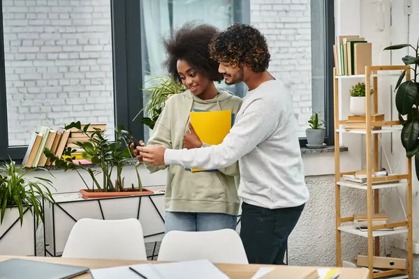 Una pareja multicultural absorta en ver contenido en un teléfono celular en un espacio de coworking moderno. - foto de stock