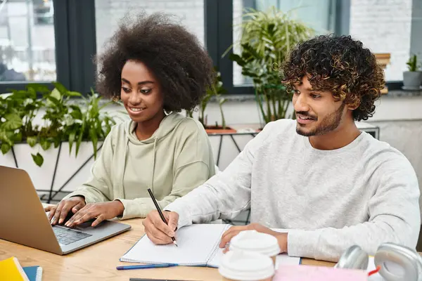 Two people, representing cultural diversity, sit at a table with a laptop, engaged in collaborative study. — Stock Photo