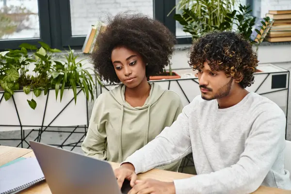 A diverse group of students working on a laptop together at a table in a modern coworking space. — Stock Photo