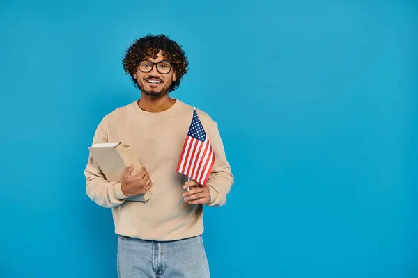 Ein Mann hält stolz ein Buch und eine amerikanische Flagge vor blauem Hintergrund in einem Atelier. — Stockfoto