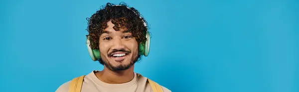 Homem indiano feliz usando fones de ouvido e sorrindo no fundo azul — Fotografia de Stock