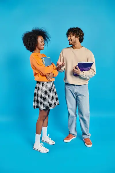 An interracial couple standing united in casual attire against a vibrant blue backdrop. — Stock Photo