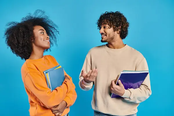 Deux étudiants interraciaux se tiennent sur un fond bleu dans un studio, mettant en valeur l'unité et la diversité. — Photo de stock