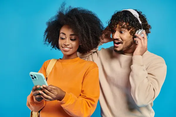 Un couple interracial en tenue décontractée debout ensemble, absorbé par la recherche d'un écran de téléphone portable. — Photo de stock