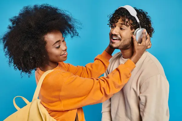 Ein Mann und eine Frau stehen zusammen mit Kopfhörern vor blauem Hintergrund und genießen die Musik. — Stockfoto