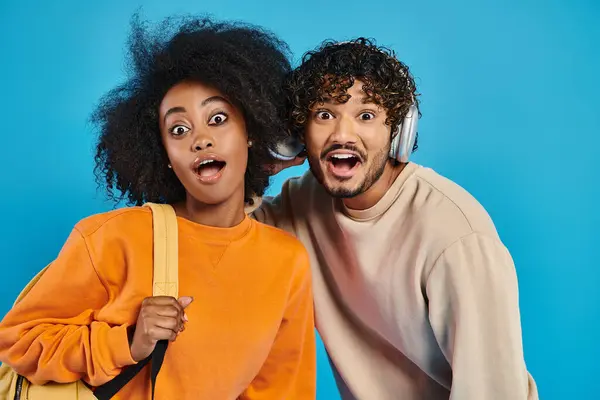 A man and a woman, interracial students, pose in casual attire against a blue backdrop in a studio. — Stock Photo