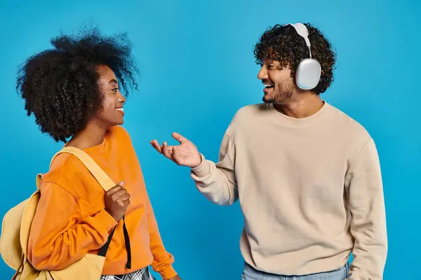 Dos estudiantes interraciales que usan atuendos casuales se paran juntos con confianza contra un telón de fondo azul en un ambiente de estudio. - foto de stock