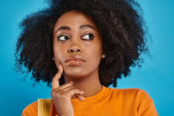 Un elegante ragazza del college afro-americano guarda verso l'alto con i suoi splendidi capelli afro su uno sfondo blu in uno studio. — Foto stock