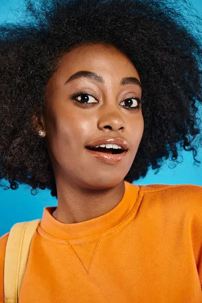 An African American college student with a voluminous afro posing confidently against a blue backdrop in a studio. — Stock Photo