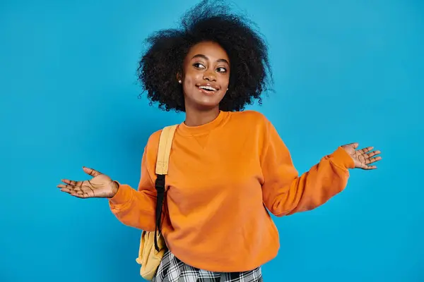 Une étudiante afro-américaine en tenue décontractée, mettant en valeur ses cheveux afro, se tient avec confiance devant un fond bleu vibrant. — Photo de stock