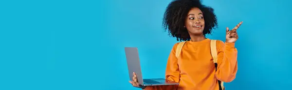 Una studentessa afroamericana indossa un abbigliamento casual e tiene un portatile su uno sfondo blu. — Foto stock