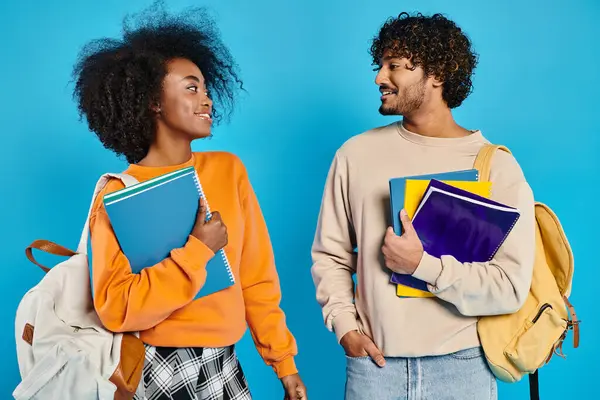 Um homem e uma mulher inter-racial segurando livros e mochilas, prontos para embarcar em uma aventura educacional. — Fotografia de Stock